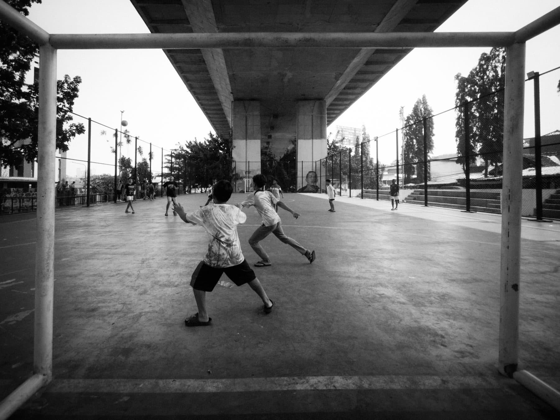 A street game under a bridge, two kids chasing the ball