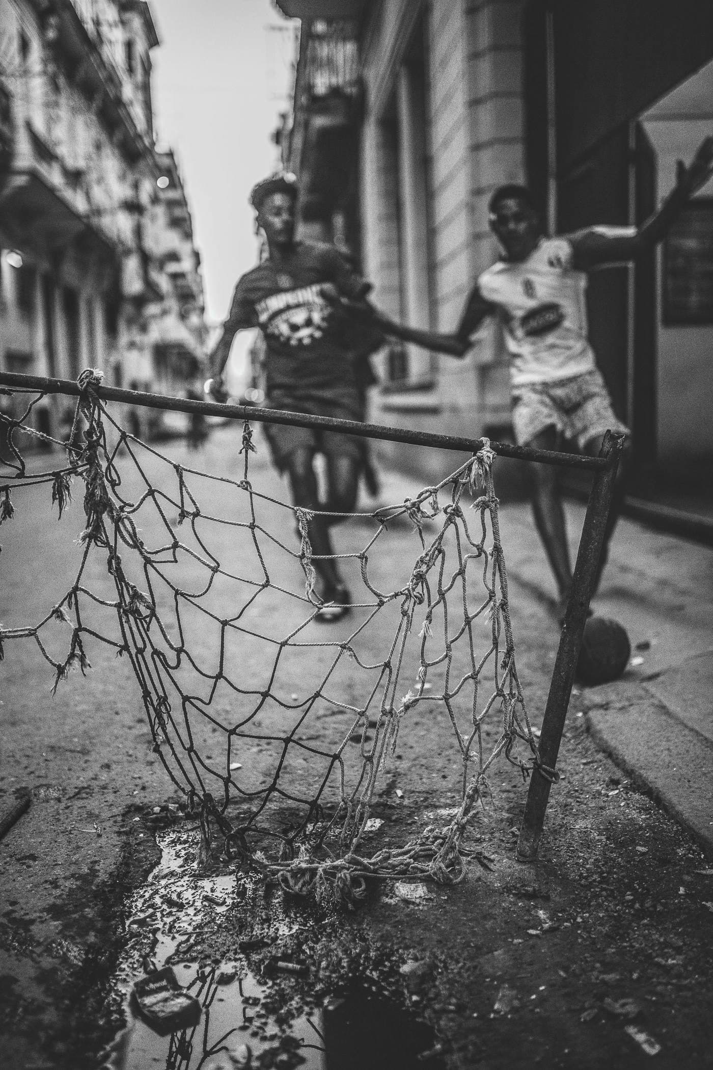A net goal tied across an old street, two players on the ball