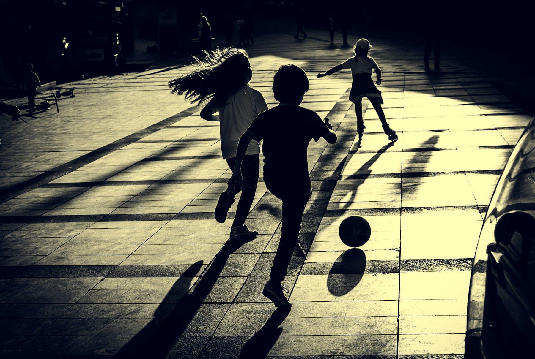 Three silhouettes playing football at night, long shadows under a hard light